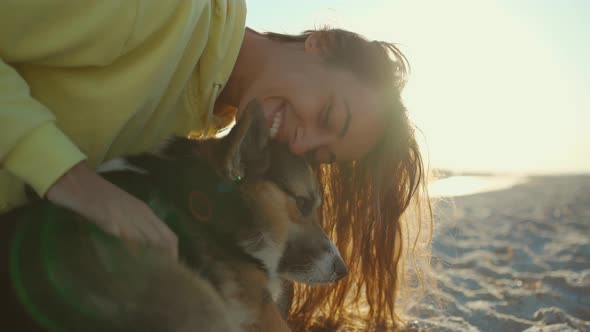 Beautiful Happy and Affectionate Laughing Girl in Yellow Hoodie at Summer Beach with Cute Pet Corgi