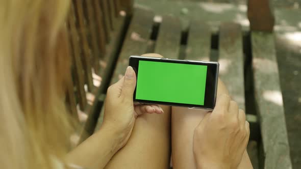 Blonde  relaxing on greenscreen smart phone display in the park 4K 2160p 30fps UltraHD footage - Blo