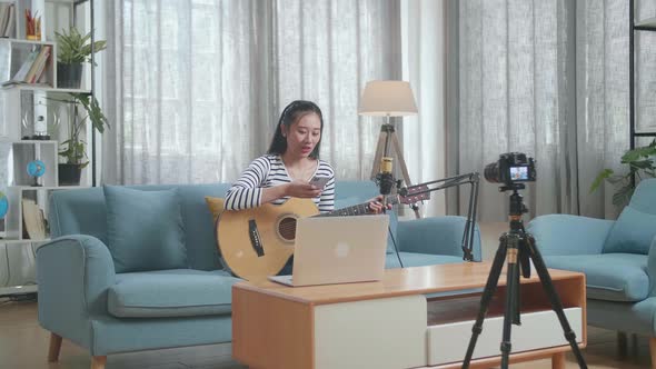 Asian Woman With A Laptop Reading Comments On Smartphone And Speaking To Camera While Live Stream