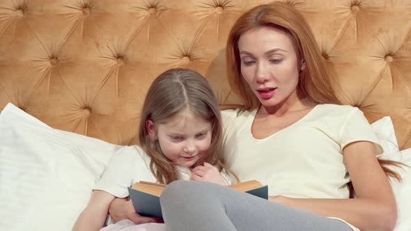 Lovely Little Girl and Her Beautiful Mom Smiling To the Camera, Reading a Book