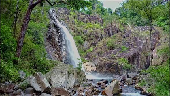 Drone Flies From Mountain River Among Boulders To Waterfall