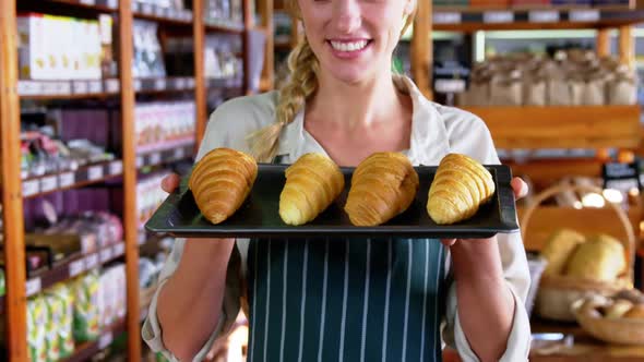 Smiling female staff holding tray of croissants in supermarket