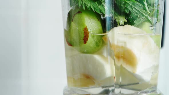 Blender Bowl with Cut Apples Kiwi and Fresh Green Leaves of Nettle