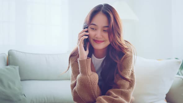 Happy young woman talking on mobile phone and smiling while sitting on the sofa at home.