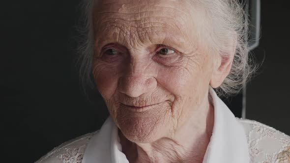 Portrait of Cute Wrinkled Grandmother Looks at Camera and Talks on Background