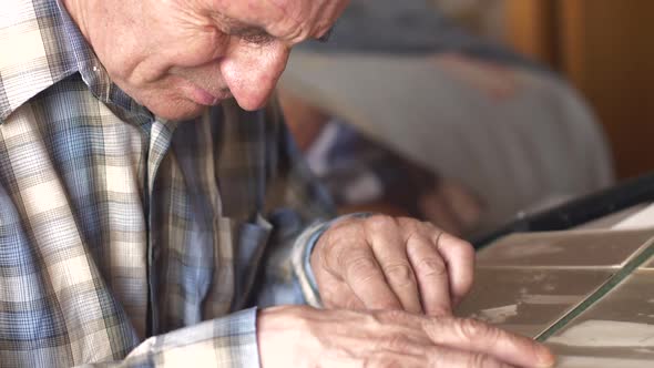 An elderly Caucasian man over 70 years old looks at a photo album while sitting at a table at home. 
