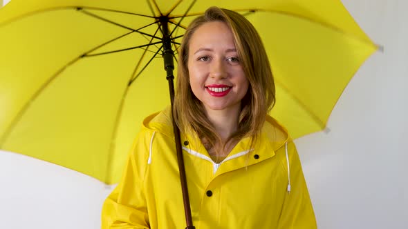 A girl in a yellow raincoat under a spinning umbrella smiles. Isolated on white background.