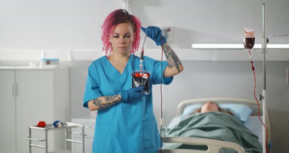 Portrait of Young Female Nurse Holding Blood Bag Looking at Camera in Hospital Ward
