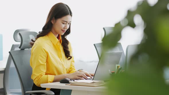 Asian woman in yellow shirt drinking coffee working with computer laptop thinking to get ideas