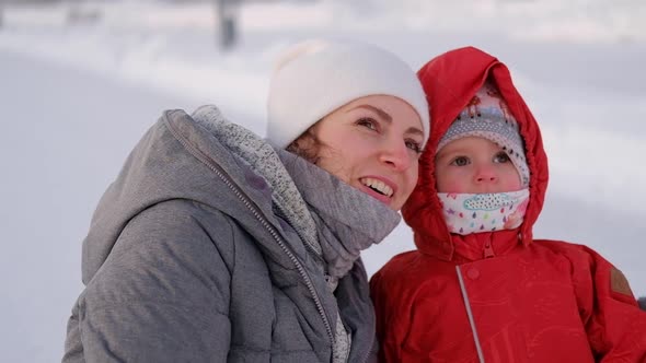 Charming mother with a child in a red winter suit walks along the street