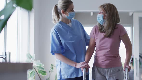 Female health worker assisting senior woman to walk with walking frame at home