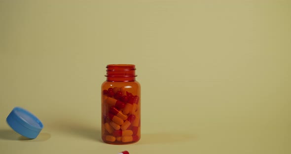 Slow motion wide shot of a bottle of pills falling and landing, the lid pops off and a single pill b