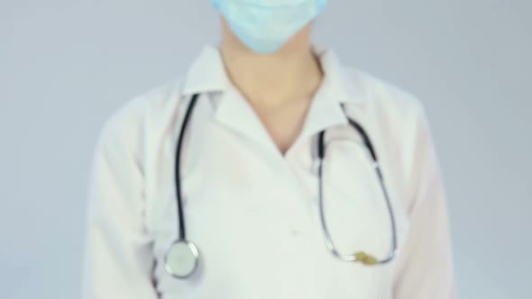 Doctor in medical face mask showing stop hand sign, warning against epidemic