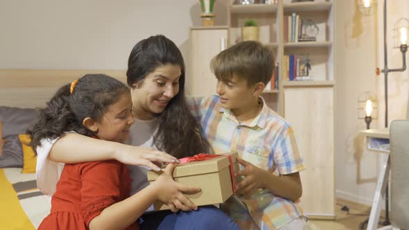 Children giving gift box to their mother. alt