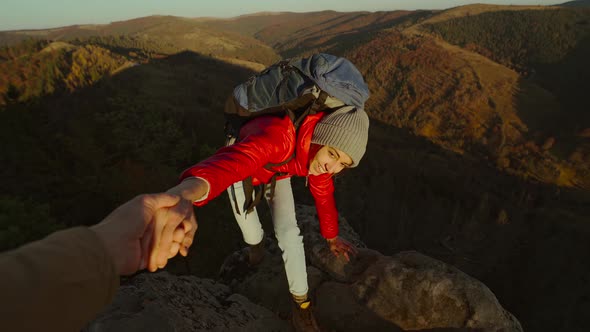 POV of Male's Hand Stretching Out and Helping Woman Hiker Reach Cliff Top By Pulling Her Up From