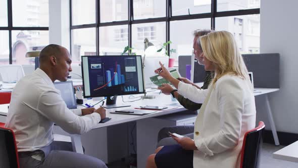 Diverse business people sitting using computer and takling at desk in office