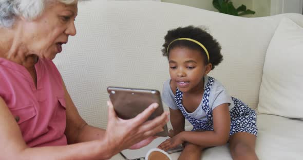 Happy african american grandmother with granddaughter using tablet in living room