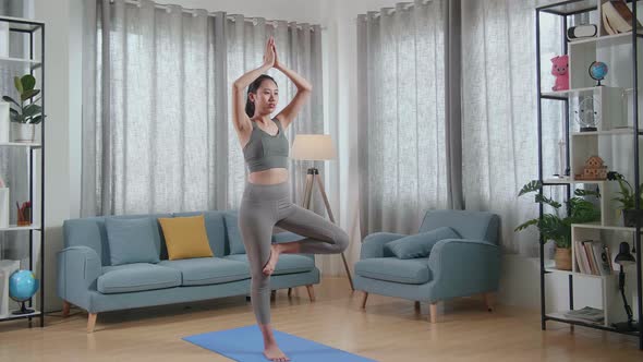 Young Asian Athletic Female In Sports Clothes Doing Yoga In Tree Pose On The Mat At Home