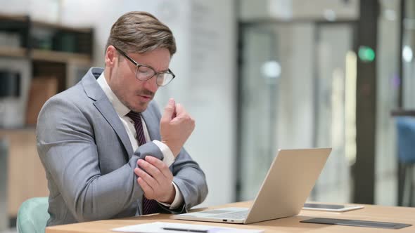 Stressed Businessman with Laptop Having Wrist Pain in Office 