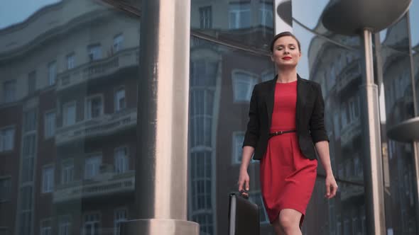 Self-confident Business Woman in a Red Dress Walks Against the Backdrop of Modern Buildings