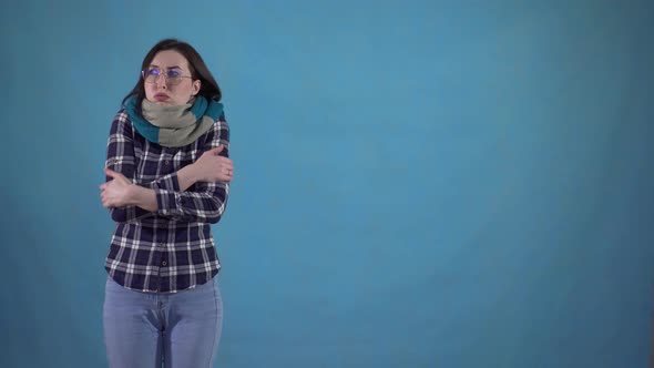 Frozen Young Woman in Scarf Can't Get Warm Standing on Blue Background