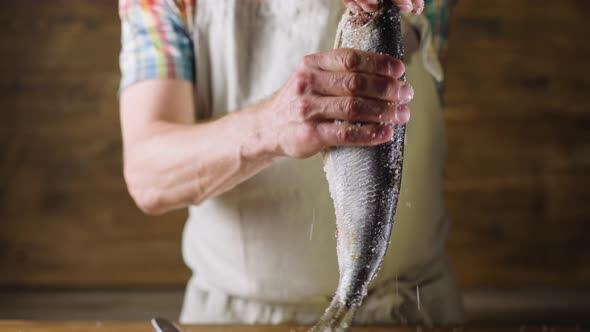 Person Removes Salt From Herring on Wooden Background