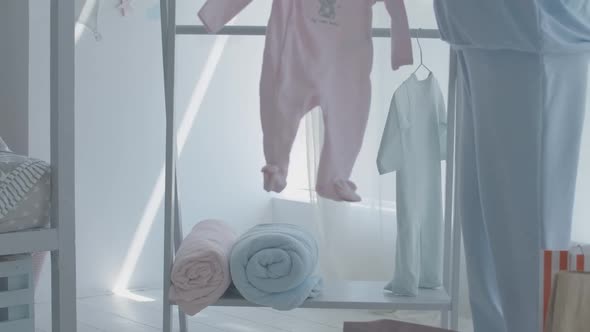 Unrecognizable Caucasian Pregnant Woman Hanging Children Clothes on Hanger in Future Baby Room
