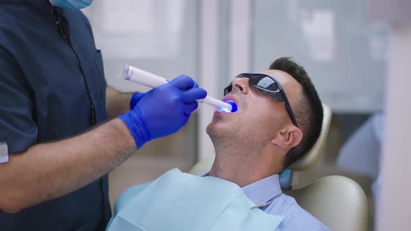 Caucasian Brunette Man in Dentist Chair with Unrecognizable Doctor in Gloves Using Ultraviolet