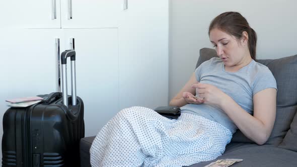 Single Woman Is Counting Her Money in Hotel Room Sitting on Sofa with Suitcase.