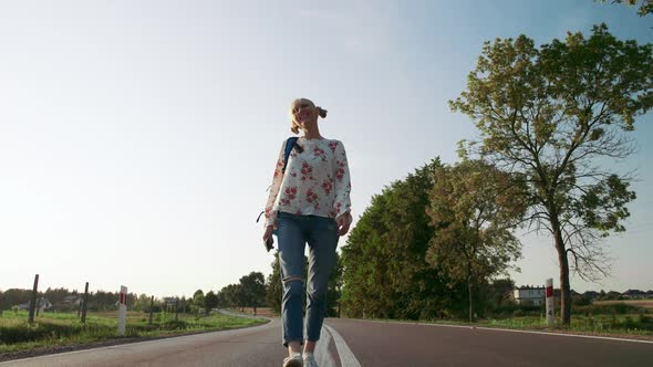 Woman with Backpack Walking on Countryside Road.