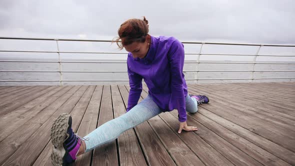 Close Up View Athletic Woman Stretching Her Legs Before a Jog on the Beach By the Sea Early in the