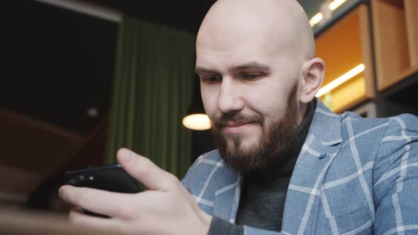 Business Man in a Suit Sitting in a Cafe Works at a Laptop and Surfs the Phone