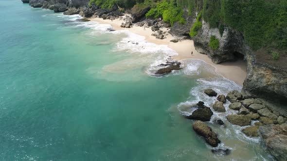 Aerial view of sandy beach with people under the rocky cliffs in Bali, Indonesia