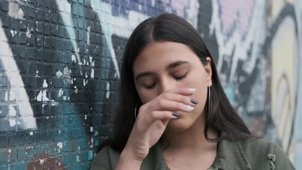 a Young Brunette Girl Stands Near a Wall with Graffiti Runs Her Hand Through Her Hair and Looks Away