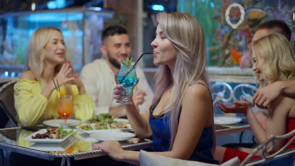 Side View of Gorgeous Confident Woman Drinking Cocktail with Blue Curacao Liquor Looking at Camera