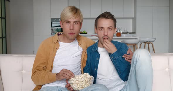 Two LGBTQ Men Watching Horror Movie Film on TV and Eating Popcorn at Home