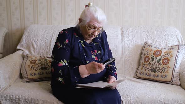 Elderly woman reads a newspaper while sitting on a sofa