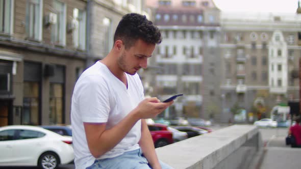 Handsome Young Man in a White Tshirt in the Center of the Old City with a Smartphone in His Hand