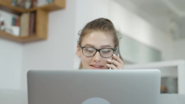 Student Girl Talking Mobile Cell Phone Smile and Using a Laptop at Home, Chatting in Social Networks