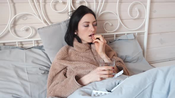 Sick Woman Laying in Bed and Taking in Pills