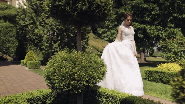 Beautiful Lovely Stylish Bride in White Wedding Dress and Veil Walking in Park and Waiting for Groom