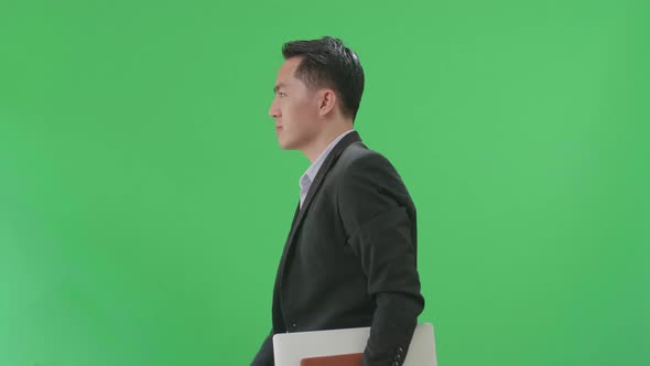 Side View Of Asian Business Man Holding Book And Document While Walking On Green Screen