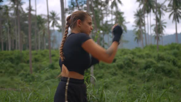 Female Athlete Practices Hitting with Hands and Feet Girl Training Among Palm Trees in the Morning