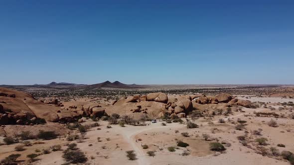 People are walking and cars are driving near the huge rocks of the desert Erongo