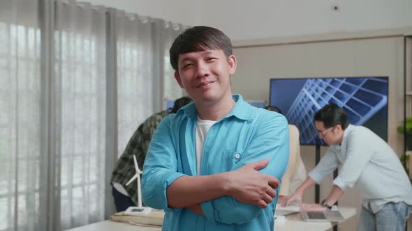 Smiling Asian Man Engineer Crossing His Arms To Camera While His Colleagues Are Discussing Work