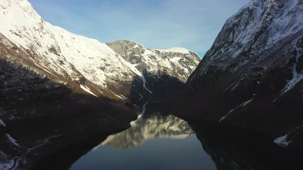 Early morning above Unesco listed Naeroyfjord - Aerial flying forward against Bakka in shadow landsc