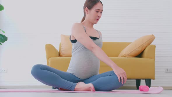 Beautiful young Asian pregnant woman in sportswear is doing yoga at home.