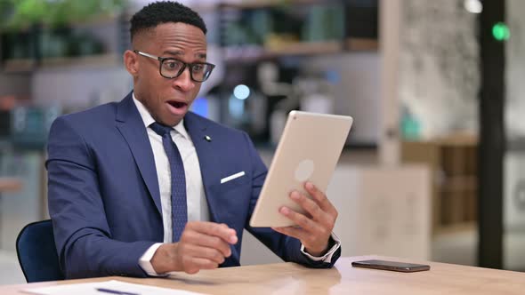 African Businessman Celebrating Success on Tablet in Office 