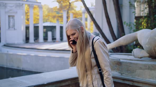 A Happy Young Girl Is Talking on a Mobile Phone in the Autumn Park of the City
