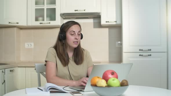 Young woman in headphones working on a laptop in the kitchen.